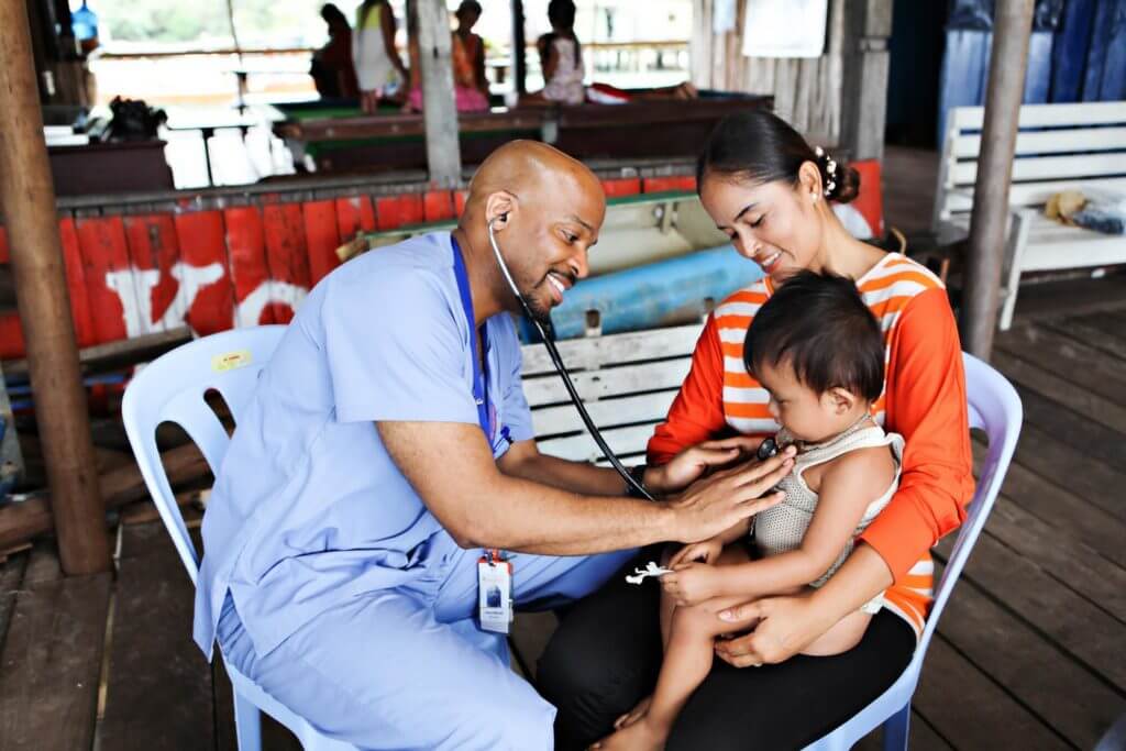 Photo of one of IMR's volunteer doctors checks the heartbeat of a child as he sits on his mother's lap